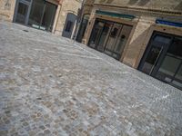 the sidewalk is paved with stones and has a bench in front of it, with no people inside