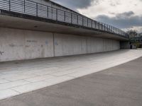 the skate boarder is balancing his board against a wall in an empty concrete space