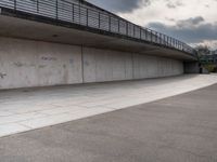 the skate boarder is balancing his board against a wall in an empty concrete space