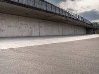 the skate boarder is balancing his board against a wall in an empty concrete space