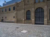 the sidewalk is paved with stones and has a bench in front of it, with no people inside