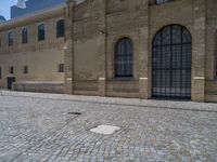 the sidewalk is paved with stones and has a bench in front of it, with no people inside