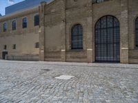 the sidewalk is paved with stones and has a bench in front of it, with no people inside