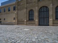 the sidewalk is paved with stones and has a bench in front of it, with no people inside