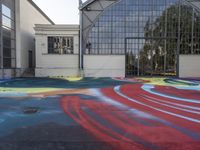 a colorful skateboard is sitting on the pavement of an empty parking lot that has painted and a large building with many windows