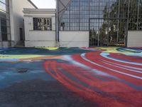 a colorful skateboard is sitting on the pavement of an empty parking lot that has painted and a large building with many windows