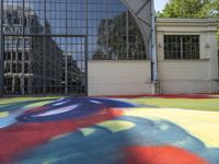 a person sitting down on a colorful floor next to an air ball field in front of a building