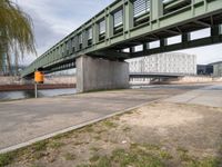 the yellow bin under the bridge is near the water's edge and the sidewalk and the path