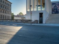 empty street lined with cement buildings next to a tall building with a staircase up to it