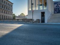 empty street lined with cement buildings next to a tall building with a staircase up to it