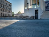 empty street lined with cement buildings next to a tall building with a staircase up to it