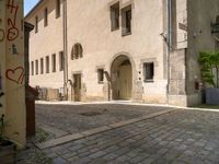 a stone road next to two tall brick buildings with doors and windows on them, one in the middle of a brick patio