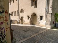 a stone road next to two tall brick buildings with doors and windows on them, one in the middle of a brick patio