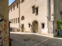 a stone road next to two tall brick buildings with doors and windows on them, one in the middle of a brick patio