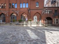 an empty brick courtyard with benches and steps leading up to the entrance, with several windows on each side