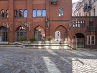 an empty brick courtyard with benches and steps leading up to the entrance, with several windows on each side