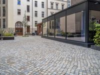 an empty parking lot with plants in the ground and on the side of the building, there is an enclosed area and windows