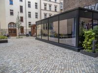 an empty parking lot with plants in the ground and on the side of the building, there is an enclosed area and windows