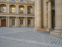 a courtyard with a building on the other side and a large white building with many windows