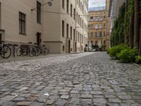 an empty brick road between buildings with bicycles parked on it's sides between the blocks