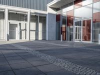 an empty sidewalk with large glass doors and no people walking down it next to a building