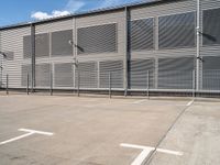 a white parking lot with a cross and street lights on it's side by some building with a fence and some blue sky