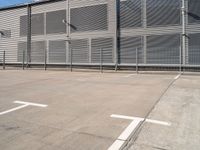 a white parking lot with a cross and street lights on it's side by some building with a fence and some blue sky