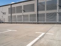 a white parking lot with a cross and street lights on it's side by some building with a fence and some blue sky