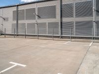 a white parking lot with a cross and street lights on it's side by some building with a fence and some blue sky