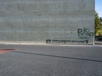 a view of a bench in front of a wall, with graffiti on it, near a park bench and fence