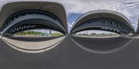 several curved shaped structures on a paved surface beneath a cloudy blue sky, showing the way to an urban area