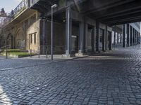 the sidewalk under an elevated bridge with columns and street lights, as well as street lights