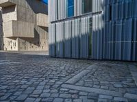 cobblestone driveway surrounded by modern buildings on sunny day with sun reflecting onto the windows