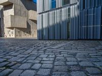 cobblestone driveway surrounded by modern buildings on sunny day with sun reflecting onto the windows