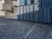 cobblestone driveway surrounded by modern buildings on sunny day with sun reflecting onto the windows