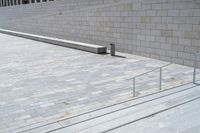 a concrete bench and railing outside an art gallery, looking down the stairs into a large brick courtyard