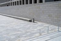 a concrete bench and railing outside an art gallery, looking down the stairs into a large brick courtyard