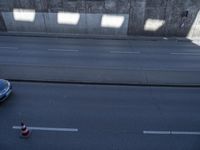 cars and a truck drive by a concrete wall on a street with multiple orange cones