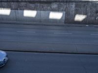 cars and a truck drive by a concrete wall on a street with multiple orange cones