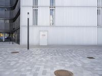 a parking space has two drains in front of a building with glass windows and a large iron manhole