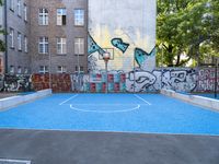 an outdoor basketball court surrounded by a bunch of other graffiti painted buildings in the background