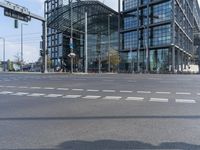 a view of a street in front of a tall glass building near traffic lights and a bike path