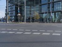 a view of a street in front of a tall glass building near traffic lights and a bike path