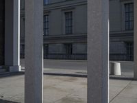 a street is lined with gray stone pillars and several buildings are in the background, all separated by gray concrete