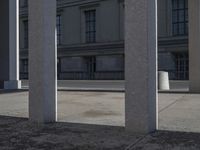 a street is lined with gray stone pillars and several buildings are in the background, all separated by gray concrete