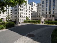 a blocky area with many apartment buildings and trees in the background, the street leads to a gate that leads to a private park on either side of one