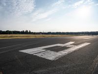 a runway at an airport on the sunny day with the sun shining through clouds above