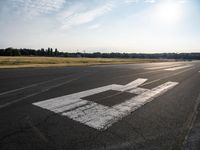 a runway at an airport on the sunny day with the sun shining through clouds above