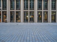 an empty brick courtyard area with two stone columns and two arched windows in the background