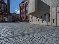 cobblestone driveway surrounded by modern buildings on sunny day with sun reflecting onto the windows